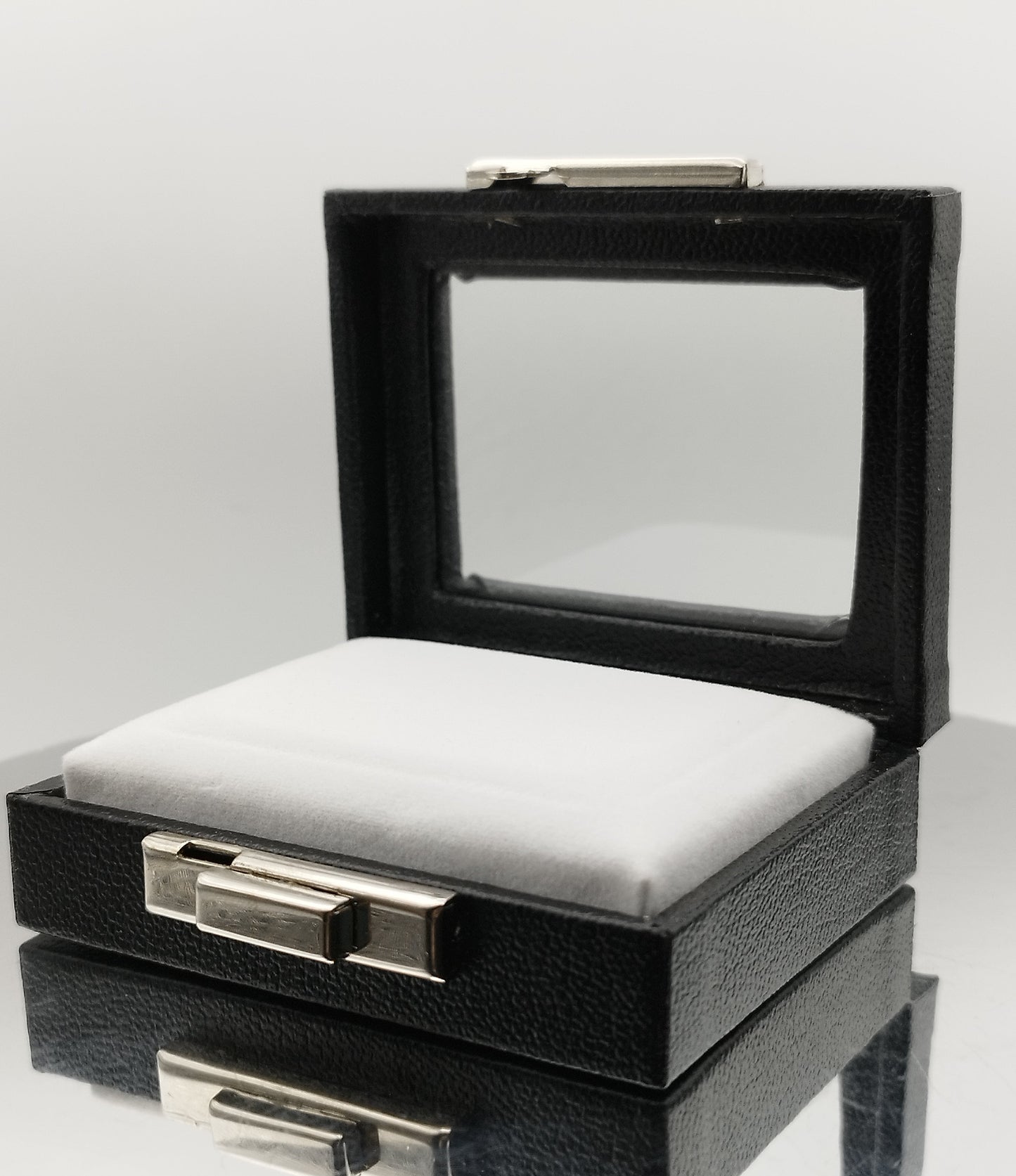 Leather-like black box with metal clasp, transparent top window, and white padded cushion. (7,5 * 6 * 2,5 cm)