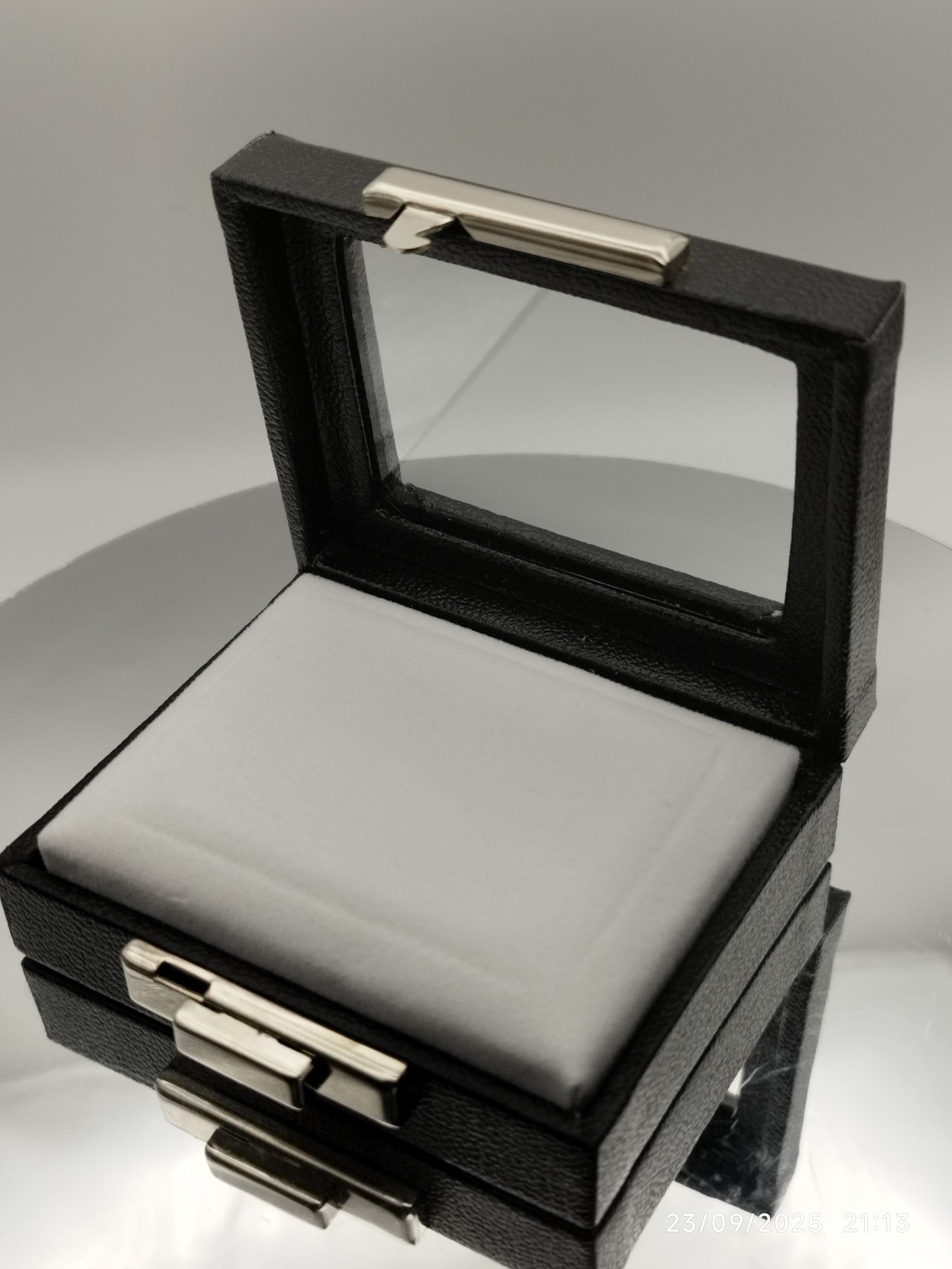 Leather-like black box with metal clasp, transparent top window, and white padded cushion. (7,5 * 6 * 2,5 cm)