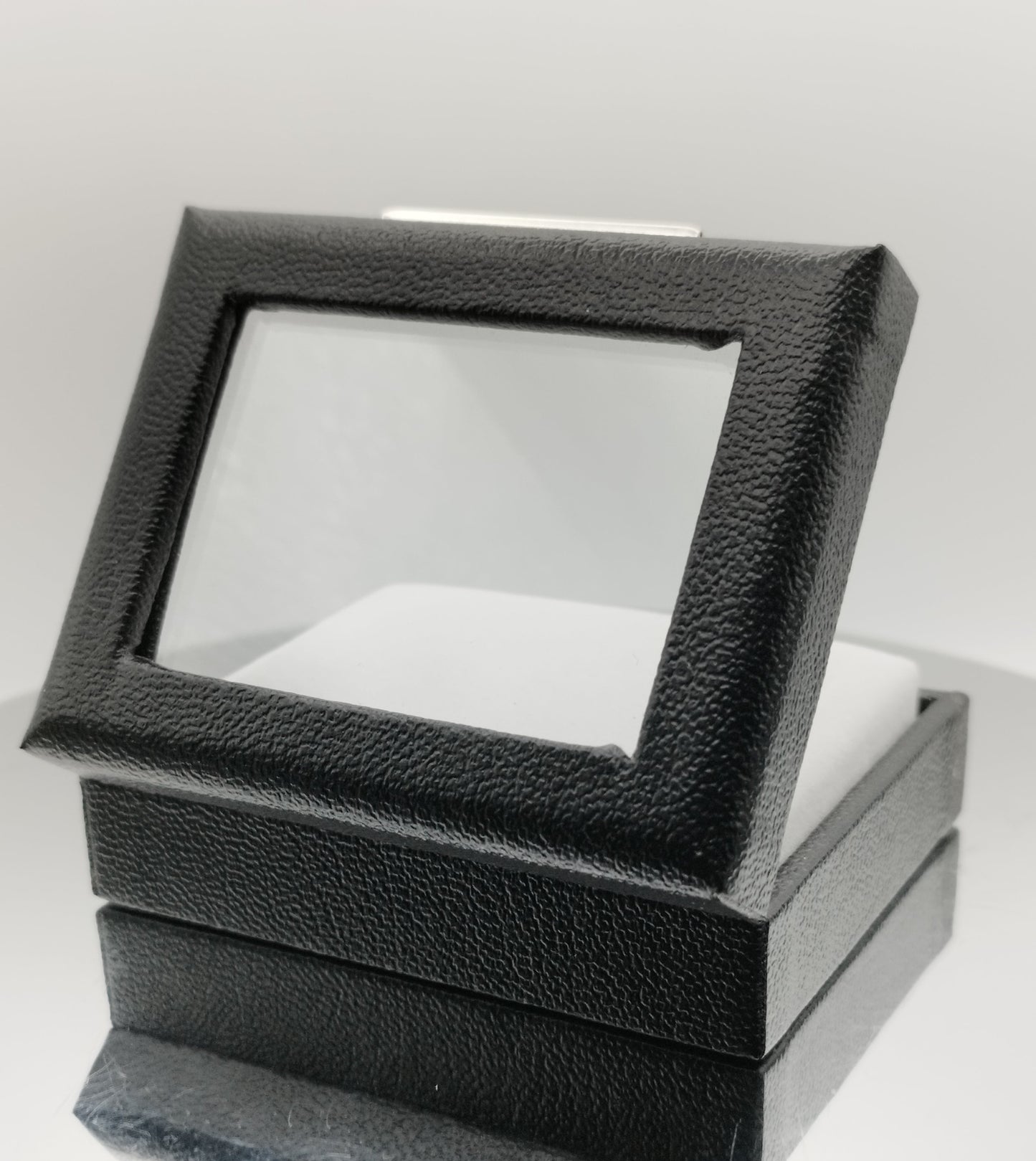 Leather-like black box with metal clasp, transparent top window, and white padded cushion. (7,5 * 6 * 2,5 cm)