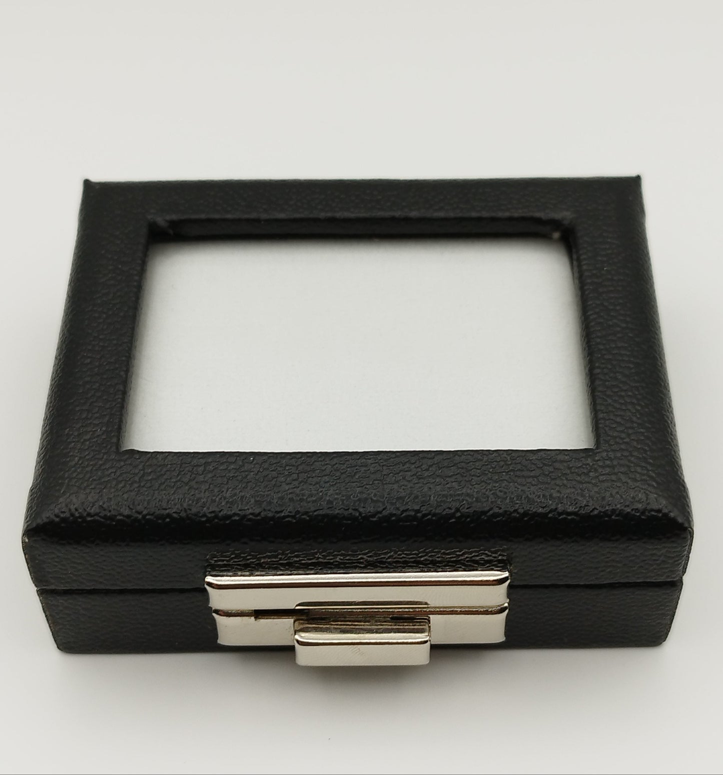 Leather-like black box with metal clasp, transparent top window, and white padded cushion. (7,5 * 6 * 2,5 cm)